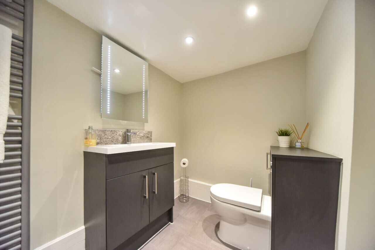 A modern bathroom with a dark vanity, a white toilet, and a mirror with LED lights.