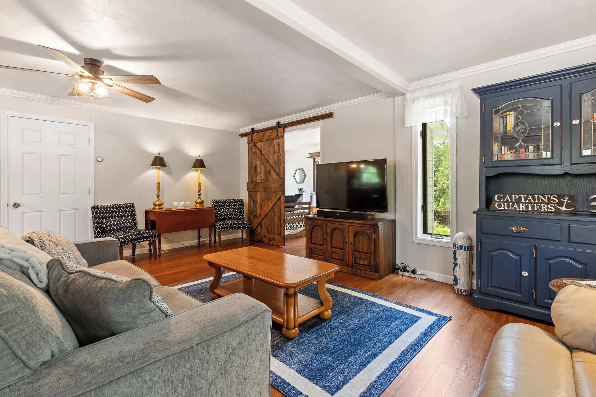A living room with a sofa, chairs, a coffee table, a TV, and a cabinet labeled 'Captain's Quarters'.