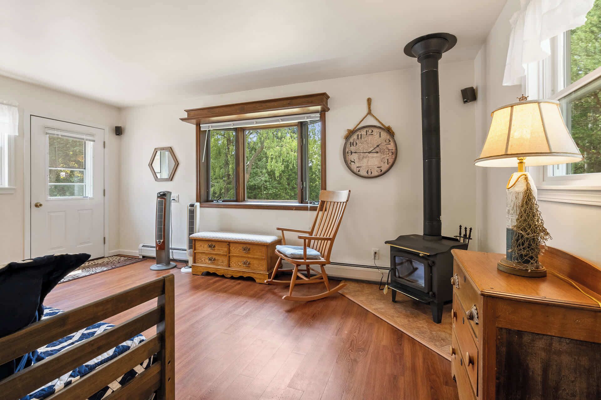 A cozy room with a wooden rocking chair, a bench, a dresser, a lamp, a wall clock, and a fireplace.