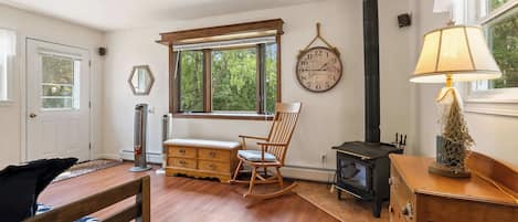 A cozy room with a wooden rocking chair, a bench, a dresser, a lamp, a wall clock, and a fireplace.