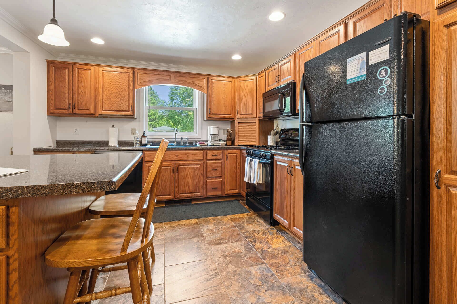 A kitchen with wooden cabinets, a black refrigerator, a stove, and a window.