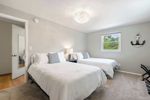 A bedroom with two beds, a chandelier, a window with a view, and a door.