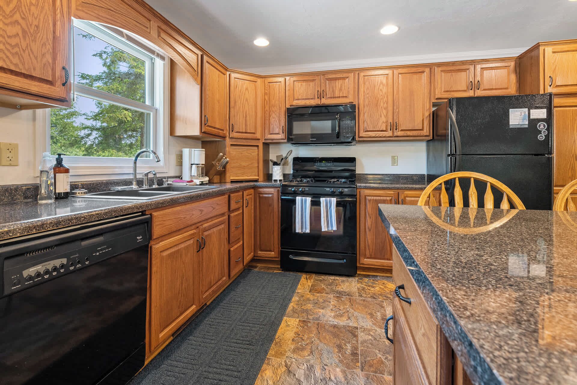 A kitchen with wooden cabinets, a granite countertop, a black stove, a microwave, and a refrigerator.