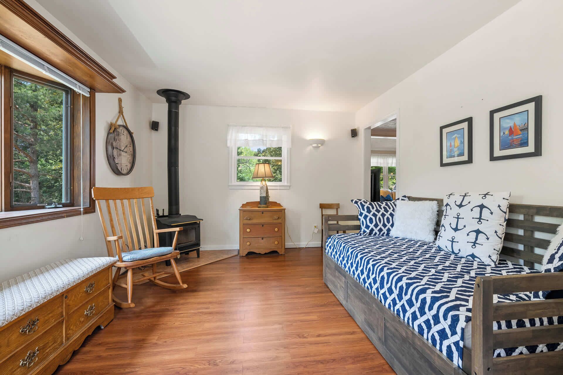 Une chambre à coucher avec un lit en bois, une commode en bois, un fauteuil à bascule, une cheminée et une fenêtre donnant sur des arbres.