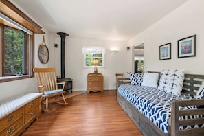 A bedroom with a wooden bed, a wooden dresser, a rocking chair, a fireplace, and a window with a view of trees.