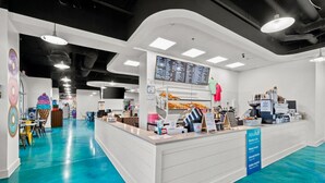 A modern cafe with a bright interior, a counter with various food items, and a menu board above. - Luxury 3BD Calypso Gulf Views! Free Beach Chairs Service for 4 (Panama City Beach)