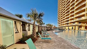 A poolside area with lounge chairs, a building with a light green facade, and a large hotel structure in the background. - Luxury 3BD Calypso Gulf Views! Free Beach Chairs Service for 4 (Panama City Beach)