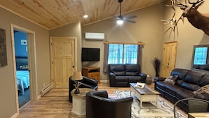 A spacious living area with a high ceiling, wooden flooring, a ceiling fan, a mounted deer head, and a large window. - Hunters Home (Brule)