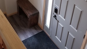 A hallway with a wooden bench, a coat rack, and a door with a peephole. - Hunters Home (Brule)