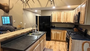 A modern kitchen with wooden cabinets, a black refrigerator, and a large island. - Hunters Home (Brule)