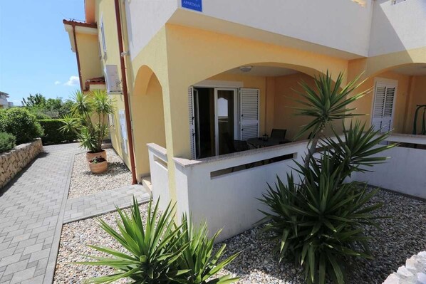 Um edifício com fachada amarela, área de recepção com balcão e cadeiras, e plantas em vasos.