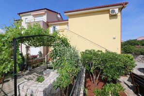 Un immeuble résidentiel à la façade jaune, doté d’un chemin bordé de pierres et agrémenté de diverses plantes.