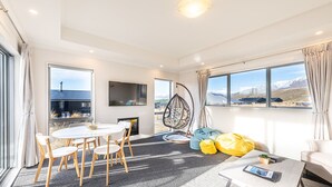 Un salon moderne comprenant un coin repas, de grandes fenêtres, un fauteuil suspendu et un canapé agrémenté de poufs.
