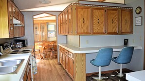Cocina con armarios de madera, encimera blanca y dos sillas azules.