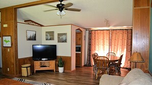 Una sala de estar con televisor, muebles de madera, ventilador de techo y un comedor con sillas y mesa.