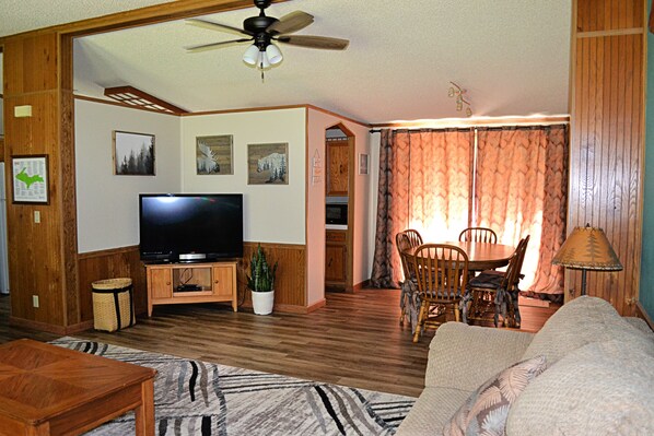 A living room with a television, wooden furniture, a ceiling fan, and a dining area with chairs and a table.
