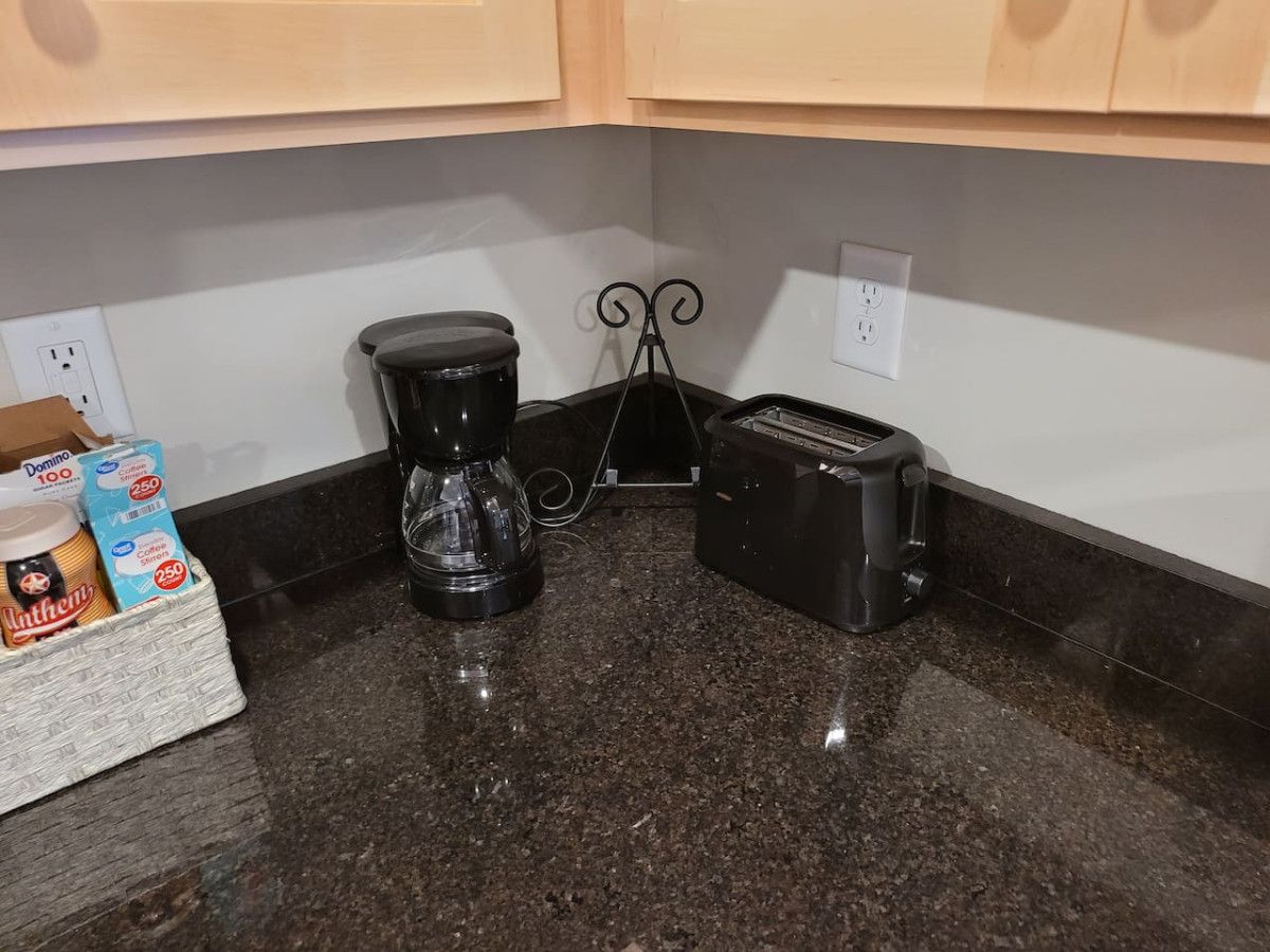 A kitchen with a coffee maker, toaster, and a basket containing Dominos and coffee.