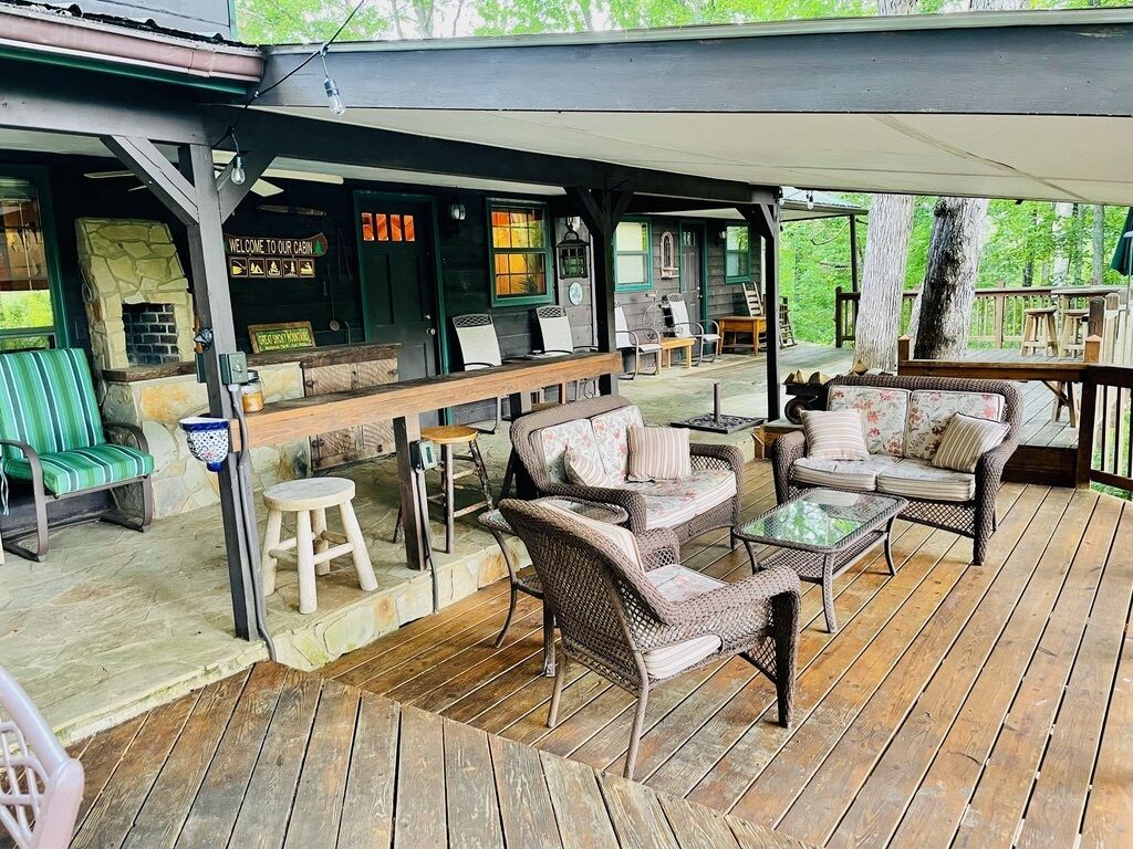 An outdoor patio with wicker furniture, a stone fireplace, and a bar area.