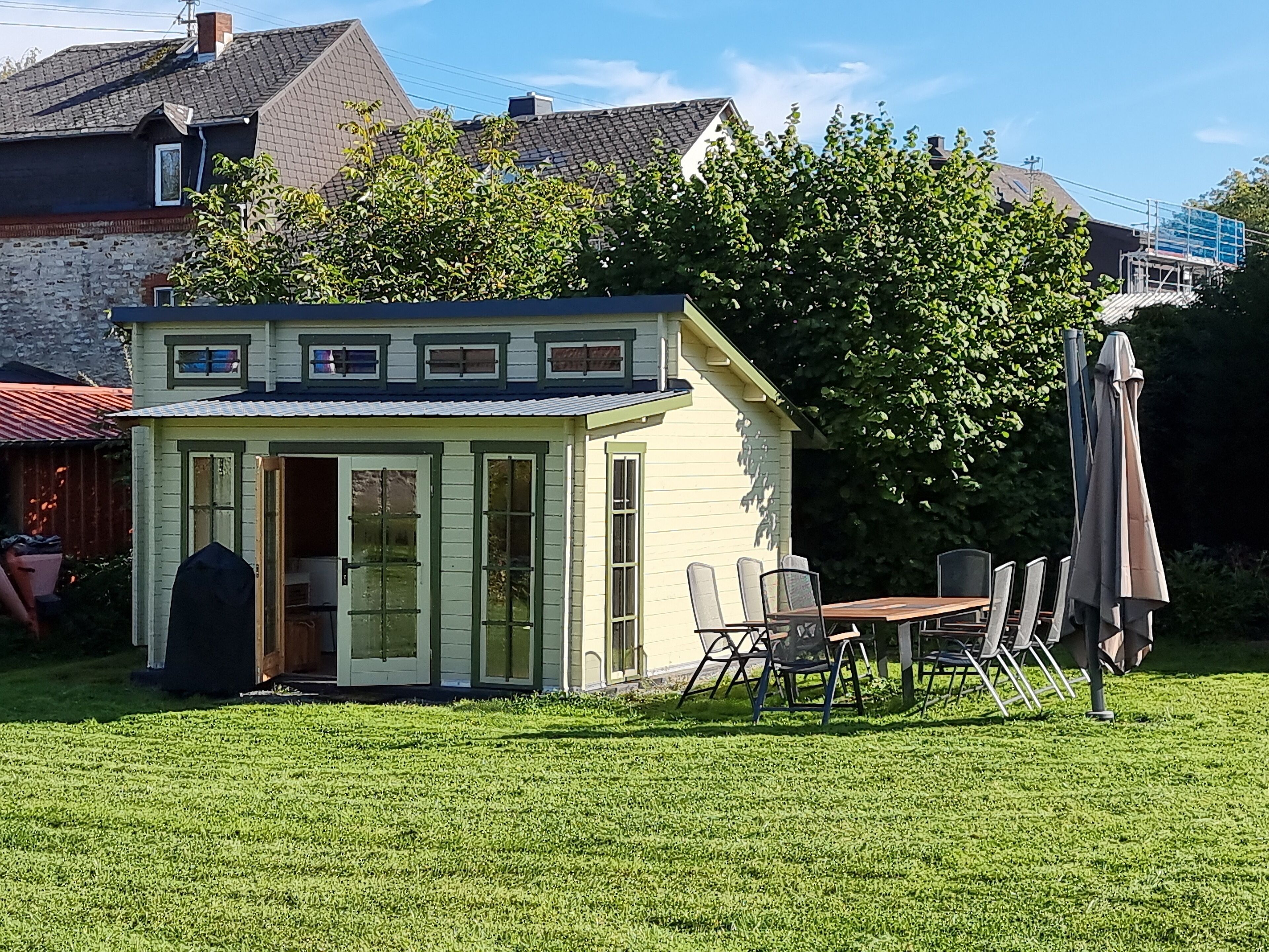 Ein kleines, eingeschossiges Haus mit grüner Fassade und einer überdachten Terrasse.