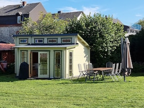 Uma casa pequena, térrea, com fachada verde e varanda coberta.