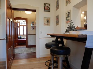 Um quarto com porta de madeira, um banquinho pequeno, uma mesa e cartazes fixados na parede.