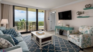 A living room with a sofa, armchair, coffee table, and a TV. There's a balcony with a view of the ocean. - Updated Beachfront Condo; Resort Amenities w/Heated Pool, Wifi & Beach Gear ~Walk to Dining & Shops (Marco Island)