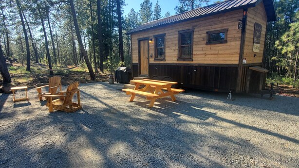 A rustic cabin with a gravel ground, wooden picnic table, and chairs.