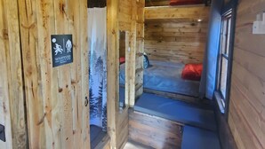 A wooden cabin interior with a bunk bed, a sign indicating a clean-up policy, and a ceiling-mounted smoke detector.