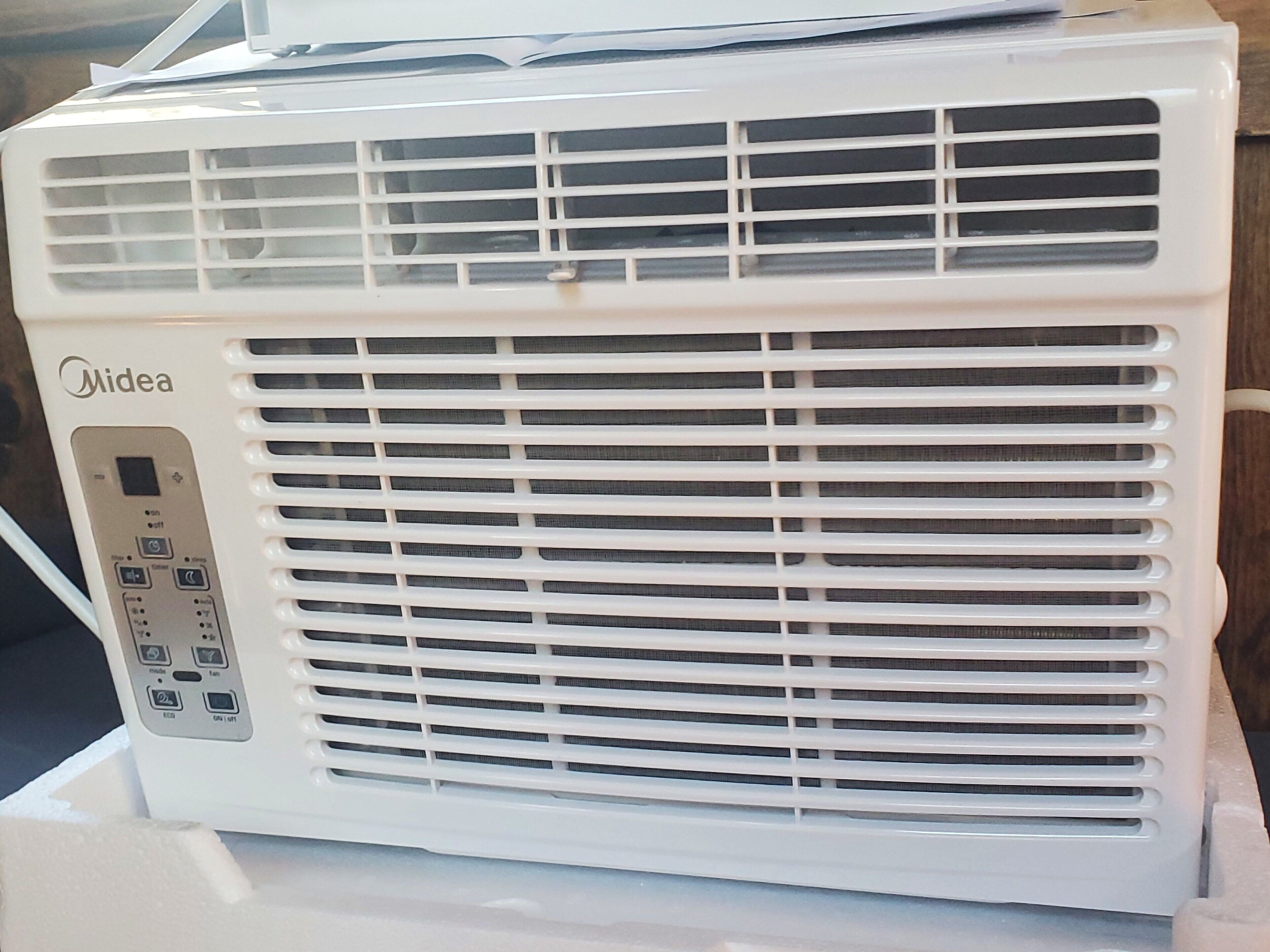 Un equipo de aire acondicionado Midea blanco con un panel de control en el lado izquierdo.