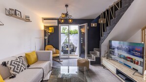 A modern living room with a sofa, coffee table, and TV. There is a staircase and a balcony with plants. - Magnificent new villa with swimming pool 6 travellers (Valros)
