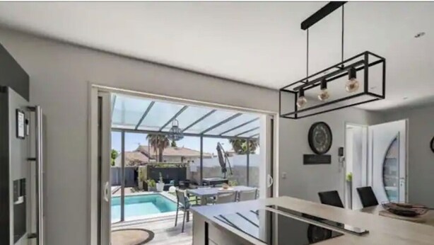 A modern kitchen with a large island, a dining area, and a view of a backyard with a pool. - Magnificent new villa with swimming pool 6 travellers (Valros)
