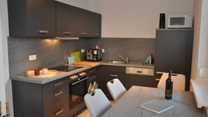 A modern kitchen with dark cabinets, a microwave, a coffee maker, and a wine bottle on the counter. - 3 Zimmer Erdgeschoss - Fewo Ferienhaus Müritzglück - Ferienwohnungen / Appartements - Ferienhaus (Röbel/Müritz)
