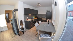 A modern kitchen with dark cabinets, a dining table, and a view of a red building outside. - 3 Zimmer Erdgeschoss - Fewo Ferienhaus Müritzglück - Ferienwohnungen / Appartements - Ferienhaus (Röbel/Müritz)