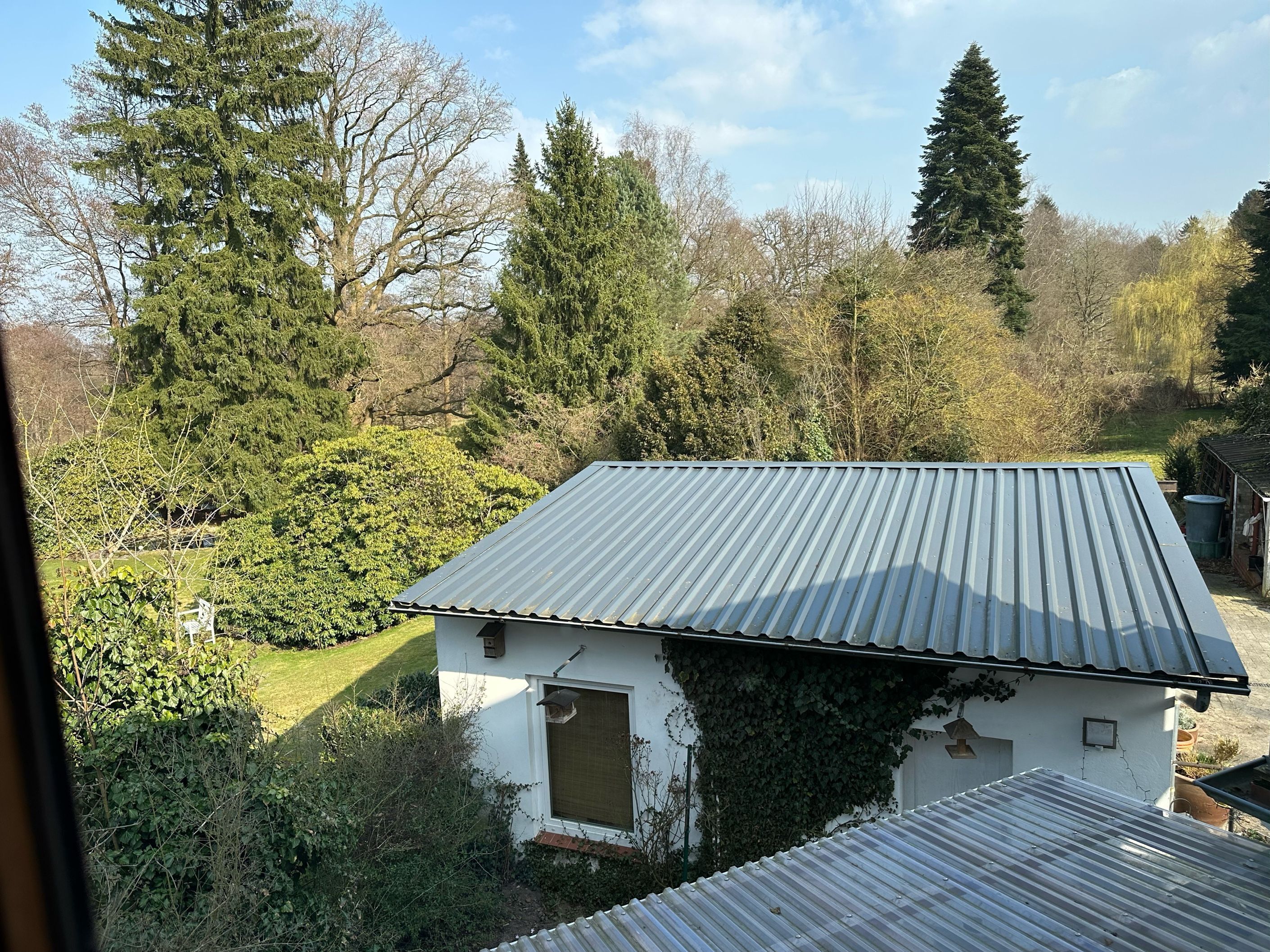 Un bâtiment blanc surmonté d’un toit en tôle ondulée, entouré de verdure et d’arbres.