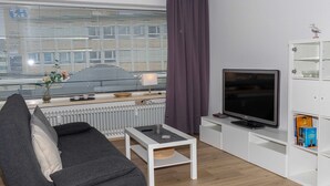 Ein modernes Wohnzimmer mit Sofa, Fernseher, Couchtisch und Bücherregal.