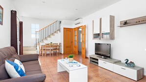 A modern living room with a sofa, coffee table, TV, and a dining area with chairs and a table.