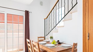 A dining area with a wooden table set for four, a staircase, and a sliding glass door with a patterned view.