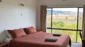 Quarto com cama grande, mesa de cabeceira, janela com vista para o campo e cortina.