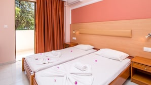 Une chambre d’hôtel avec une tête de lit en bois, deux lits avec du linge de lit blanc et des pétales de fleurs roses, une table de chevet en bois et un climatiseur fixé au mur.