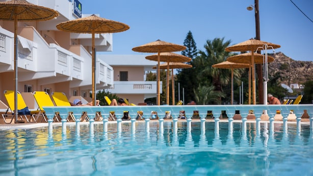Une piscine entourée de bâtiments et de palmiers, avec des chaises longues et des parasols.
