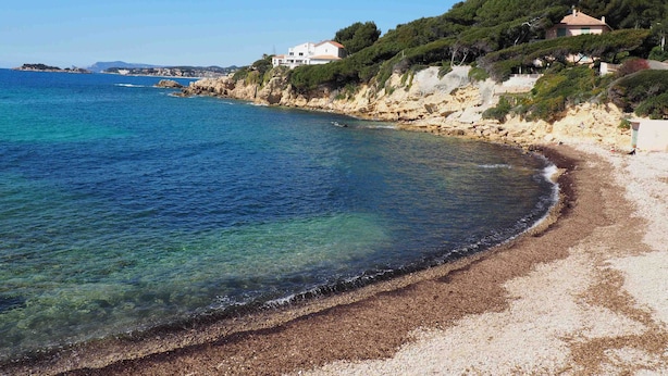Una platja costanera amb aigües blaves cristal·lines, penya-segats rocoses i edificis al vessant de la muntanya.