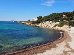 A coastal beach with clear blue waters, rocky cliffs, and buildings on the hillside. - ABSOLUTE PEACE AND QUIET, UNDER THE PINE TREES - 300m FROM THE BEACH - 2 BEDROOMS - INTERNET - PARKING (Sanary-sur-Mer)