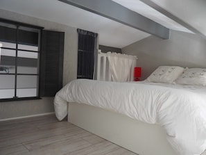 Ein Schlafzimmer mit Bett, einem Fenster mit Jalousien, einem Vorhang und einer roten Wandlampe.
