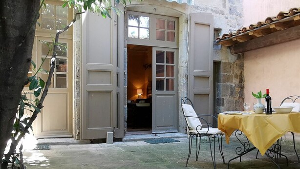 Puerta abierta que da a un espacio exterior con una mesa y sillas, una planta pequeña sobre la mesa y un árbol al frente.