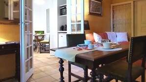 Un comedor con una mesa dispuesta para dos personas, una cocina al fondo y una puerta que da a otra habitación.
