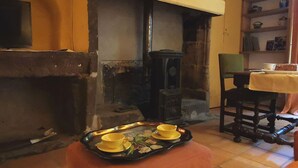 Una habitación acogedora con chimenea, una silla de madera, una mesa con mantel amarillo y una bandeja con tazas.