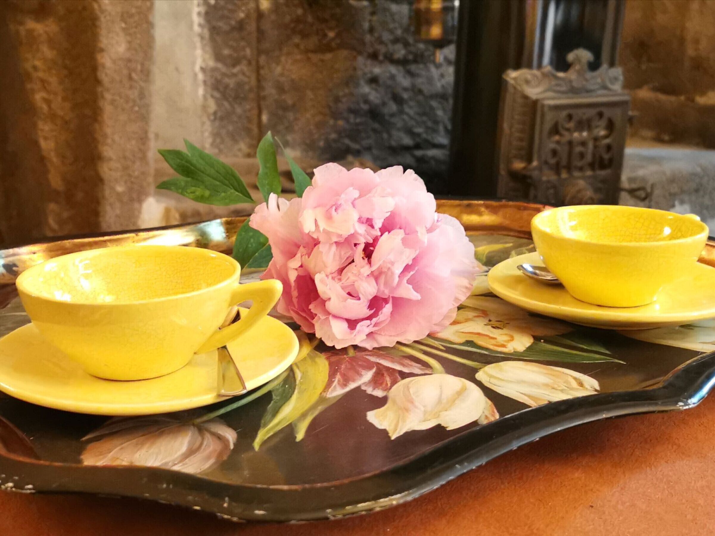 A tray with yellow cups and saucers, a pink peony, and a decorative plate with floral designs.