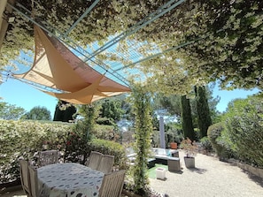 An outdoor seating area with a table and chairs, surrounded by greenery and a pergola structure. - Entire private gîte (Lédenon)