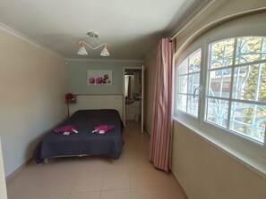 A bedroom with a bed, a bedside table, a window with curtains, a bathroom visible through an open door, and a ceiling light fixture. - Entire private gîte (Lédenon)