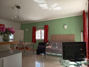 A living room with a dining area, a sofa, a TV, and a window with curtains. - Entire private gîte (Lédenon)